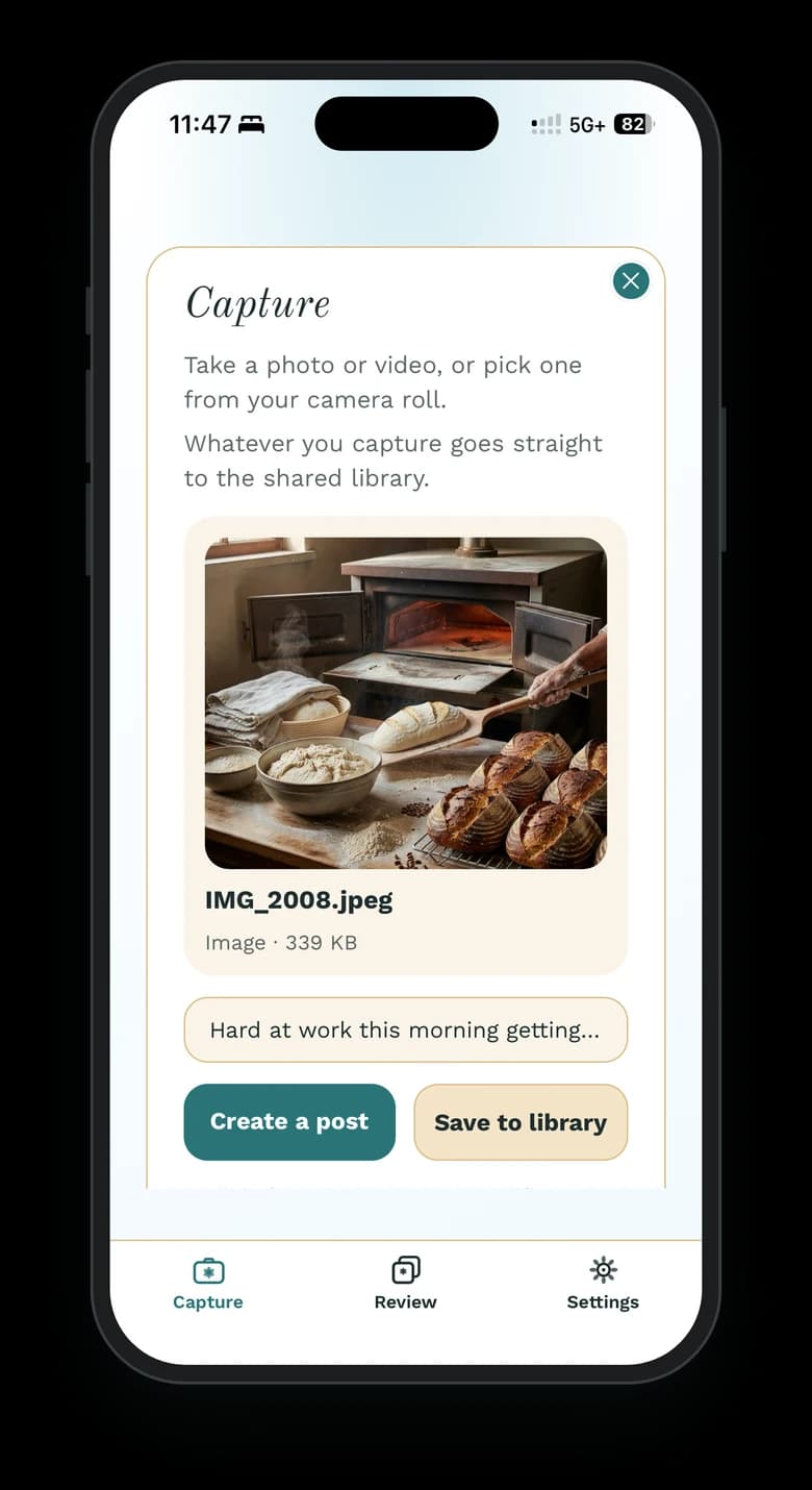 The Wallflower phone app on an iPhone, open to Capture with a just-picked photo, IMG_2008.jpeg, of a baker sliding a loaf into a wood-fired oven beside a rack of round sourdough loaves, the note “Hard at work this morning getting…”, and Create a post and Save to library buttons.